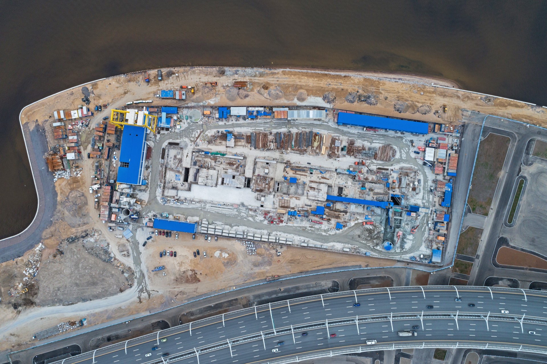 Aerial view of a large waterfront construction site with adjacent highway interchange
